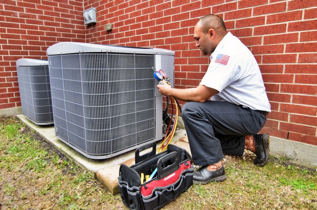 HVAC technician crouching next to outdoor AC unit during inspection.