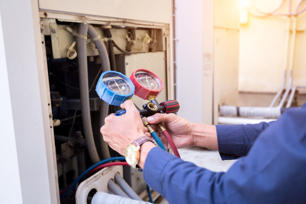 Technician using gauge tool to maintain an HVAC unit.