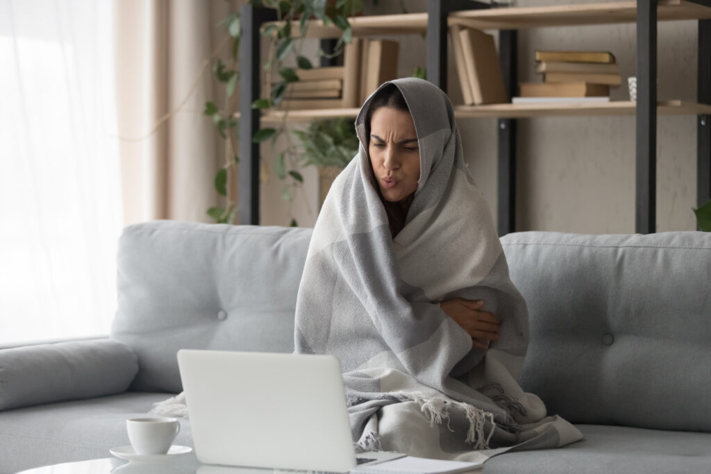 A woman sitting on a couch wrapped in a blanket.
