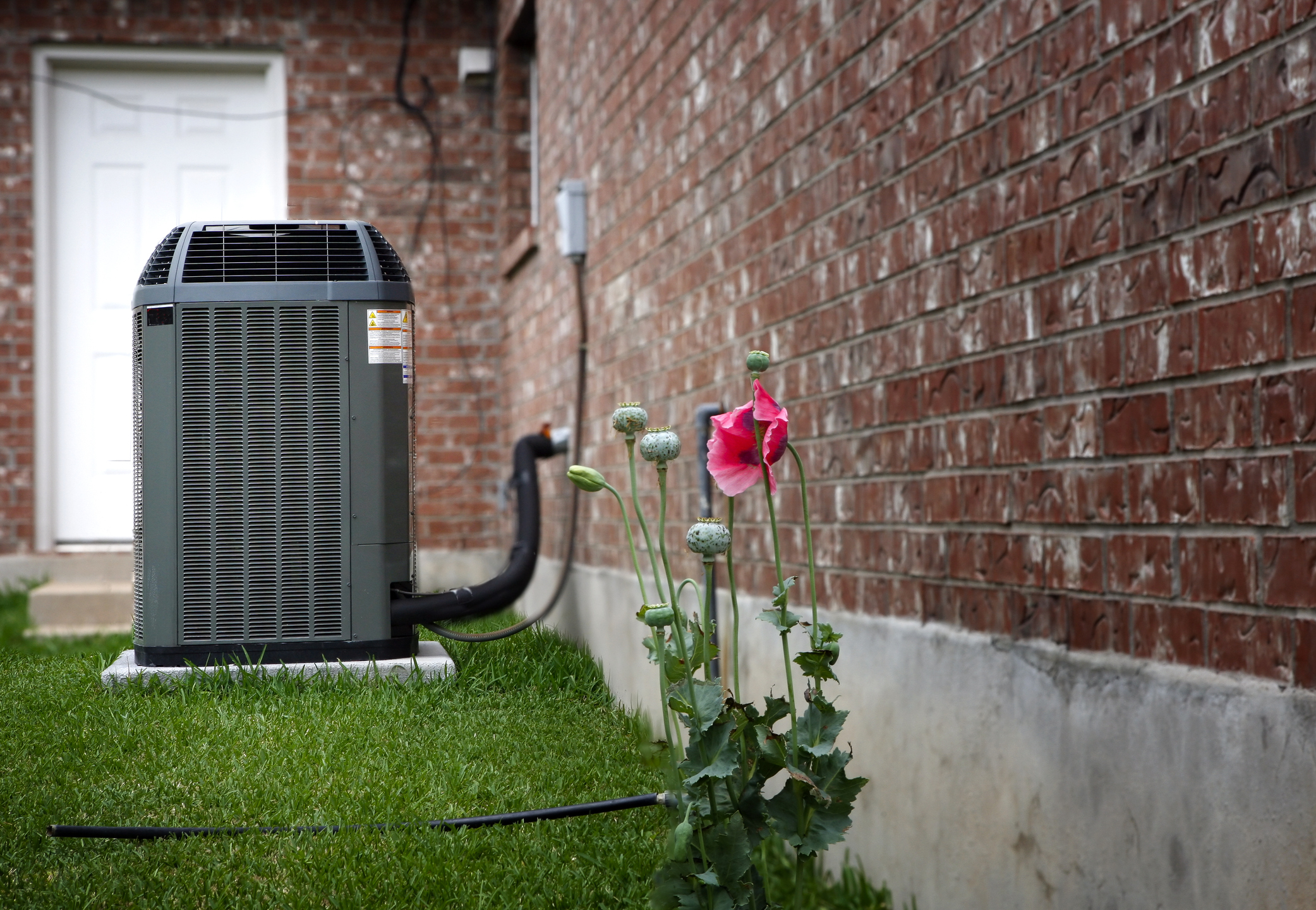 New HVAC unit set up next to a brick home, with pink flowers blooming in foreground.